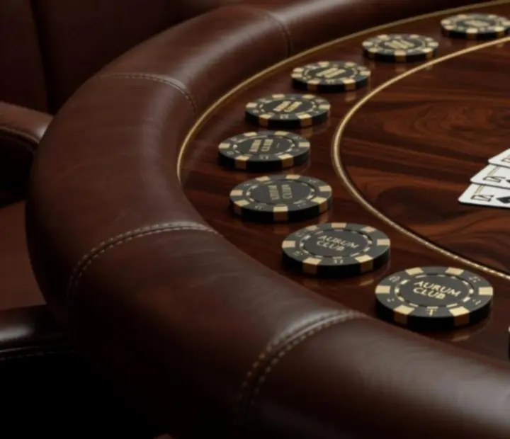 Detail luxusného pokerového stola s koženým lemovaním, žetónmi a kartami pripravenými na hru.